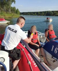zdjęcie przedstawia akwen, na środku którego, policjant sprawdza stan trzeźwości osób znajdujących się na rowerku wodnym