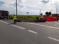 zdjęcie przedstawia skrzyżowanie, na środku którego stoi dwóch policjantów. Widać również rozbity samochód, motocykl, dwa wozy strażackie i rozłożony czerwony parawan