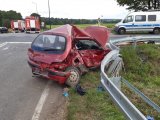 zdjęcie przedstawia samochód osobowy, który ma wgnieciony prawy bok i powybijane szyby. Na zdjęciu widać również policjanta, policyjny radiowóz i wóz strażacki.