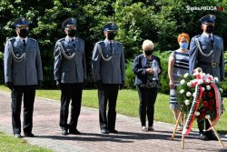 zdjęcie przedstawia ubranych w mundury galowe policjantów i dwie kobiety. Przed nimi widać wieniec