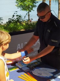 zdjęcie przedstawia policjanta, który zakłada chłopcu opaskę na rękę