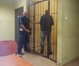 na zdjęciu widać policjanta, który wprowadza do policyjnej celi, zatrzymanego mężczyznę