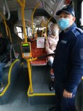 Zdjęcie przedstawia wnętrze autobusu. Przy drzwiach stoi policjant. Na fotelach siedzą pasażerowie
