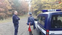 zdjęcie przedstawia parking leśny, na którym policjant rozmawia z grzybiarzem