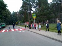 zdjęcie przedstawia przejście dla pieszych, po którym przechodzi grupa dzieci. Obok stoi policjant, który sprawdza, czy robią to prawidłowo