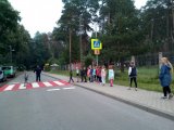 zdjęcie przedstawia przejście dla pieszych, po którym przechodzi grupa dzieci. Obok stoi policjant, który sprawdza, czy robią to prawidłowo
