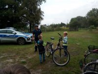 na zdjęciu widać policjanta i policyjny radiowóz oraz dwóch chłopców, pomiędzy którymi stoi rower