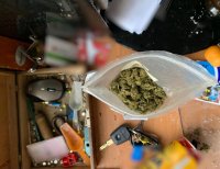 Widok z góry. Na stole widać otwarty worek strunowy wewnątrz, którego znajduje się marihuana. Obok worka, na stole leżą przeróżne rzeczy m.in kluczyk samochodowy, puszka po piwie itd.