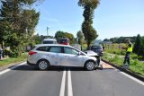 Na zdjęciu widać samochód osobowy, który stoi w poprzek drogi. Obok samochodu widać tył drugiego pojazdu biorącego udział w zdarzeniu. Obok samochodów widać policjantów wykonujących czynności.