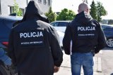 Na zdjęciu widać dwóch policjantów ubranych w kurtki taktyczne. Na plecach mają napis POLICJA Wydział Kryminalny