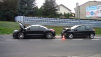 Na zdjęciu widać drogę, na poboczy której jeden za drugim, stoją dwa zniszczone peugeoty