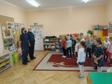 Na zdjęciu widać szkolną klasę, w której przed grupą uczniów stoi policjant i policjantka