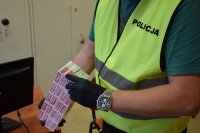 Na zdjęciu widać policjanta w kamizelce odblaskowej, który w dłoni trzyma kilka paczek nielegalnych papierosów