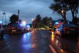 Na fotografii widać skrzyżowanie,  przy którym stoją zaparkowane policyjne radiowozy oraz wóz strażacki z włączonymi sygnałami świetlnymi. W tle zdjęcie widać strażaków oraz policjantów wykonujących czynności.