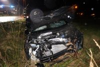 Na zdjęciu widać leżący w rowie samochód osobowy. Auto ma podniesioną do góry maskę, rozbity przód i przednią szybę.