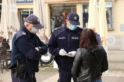 Na zdjęciu widać dwóch policjantów w maseczkach, którzy spisują dane personalne stojącej przed nimi kobiety.