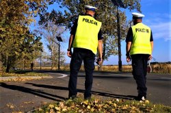 Na zdjęciu widać odwróconych tyłem, dwóch policjantów z Wydziału Ruchu Drogowego obserwujących drogę.