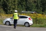 Na zdjęciu widać policjanta z drogówki, który idzie w kierunku samochodu osobowego, zaparkowanego na poboczu drogi.