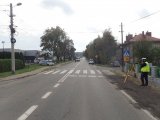 Na zdjęciu widać drogę, na której znajduje się oznakowane przejście dla pieszych. Przy drodze i na drodze widać policjantów, którzy wykonują czynności - pomiary specjalnym urządzeniem służącym do wykonywania pomiarów