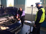 Na zdjęciu widać stację diagnostyczną, na której pracownik, specjalnym urządzeniem, sprawdza światła w pojeździe. Czynność obserwuje policjant z Wydziału Ruchu Drogowego.