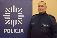 na zdjęciu dzielnicowy Miernik przy banerze z napisem policja