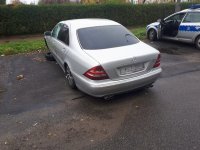 Na zdjęciu widać mercedesa zaparkowanego na osiedlowym parkingu. Samochód nie ma przedniego koła. Obok pojazdu stoi policyjny radiowóz