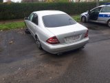 Na zdjęciu widać mercedesa zaparkowanego na osiedlowym parkingu. Samochód nie ma przedniego koła. Obok pojazdu stoi policyjny radiowóz