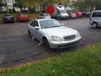 Na zdjęciu widać mercedesa zaparkowanego na osiedlowym parkingu. Auto podparte jest na cegłach, nie ma przedniego i tylnego koła od strony pasażera. W tle zdjęcia widać inne zaparkowane samochody.