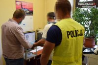 Na fotografii widać trzech mężczyzn - dwóch policjantów i zatrzymanego mężczyznę, któremu jeden z policjantów pobiera odciski palców. Odcisk palca sprawcy widać na monitorze komputera.