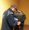 zdjecie przedstawia umundurowanego policjanta zakuwającego w kajdanki sprawcę