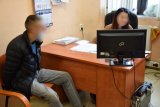 Na zdjęciu widać zatrzymanego mężczyznę siedzącego obok biurka. Po drugiej stronie biurka siedzi policjantka, która przesłuchuje sprawcę.