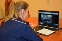 Na zdjęciu widać policjantkę, która siedzi przy stole, przed laptopem i prowadzi zajęcia profilaktyczne online. Na monitorze laptopa widać wizerunek policjantki.