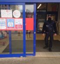 Na zdjęciu widać policjanta, który wychodzi ze sklepu wielopowierzchniowego. Na drzwiach sklepu naklejone są informacje dotyczące stosowania dystansu oraz maseczek