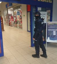 Na zdjęciu widać policjanta, który wchodzi do sklepu wielopowierzchniowego. Przed policjantem znajduje się wejście do jednego ze sklepów odzieżowych