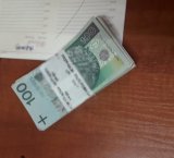 Na zdjęciu widać leżący na biurku plik 100 złotowych banknotów
