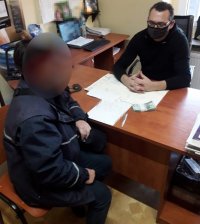 Na zdjęciu widać siedzących po obu stronach biurka, policjanta oraz listonoszkę. Na biurku leży plik banknotów.