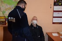 Na zdjęciu widać policjanta, który stoi obok siedzącego na krześle, zatrzymanego mężczyzny.