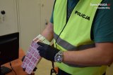 Na zdjęciu widać policjanta w kamizelce odblaskowej, który w dłoni trzyma kilka paczek nielegalnych papierosów