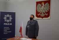 Na zdjęciu widać Pierwszego Zastępcę Komendanta Powiatowego Policji w Tarnowskich Górach mł. insp. Sławomira Bylickiego. Obok Komendanta widać wiszące na ścianie godło, biało-czerwoną flagę oraz policyjny baner.