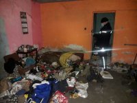 Na zdjęciu widać policjanta, który znajduje się w pomieszczeniu, w którym panuje duży bałagan - porozrzucane ubrania, puszki i słoiki
