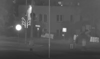 Zdjęcie czarno-białe. Na fotografii widać 4 osobową grupę, która stoi na ulicy. W tle widać budynek szkoły i plac zabaw.