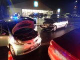 Na zdjęciu widać dwa samochody osobowe biorące udział w wypadku. W tle widać parking sklepowy, na którym znajdują się samochody oraz policyjny radiowóz