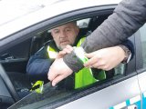 Na zdjęciu widać policjanta w radiowozie, który zakłada odblask na rękę pieszego