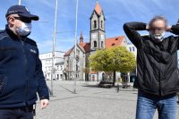 Na zdjęciu widać policjanta i mężczyznę, który poprawia maseczkę na twarzy. Zdjęcie zrobiono na Rynku w Tarnowskich Górach