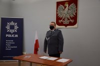 Na zdjęciu widać pełniącego obowiązki Komendanta Powiatowego Policji w Tarnowskich Górach młodszego inspektora Sławomira Bylickiego, Obok którego znajduje się biało-czerwona flaga oraz godło.