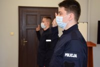 Na zdjęciu widać dwóch policjantów, którzy mają uniesione do góry palce i składają rotę ślubowania.