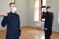 Na zdjęciu dwóch policjantów, którzy mają uniesione do góry palce i składają rotę ślubowania.