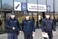 Na zdjęciu widać trzech policjantów stojących przed wejściem do Szpitala Tymczasowego MCK w Katowicach. Nad wejściem widnieje napis &quot;punkt szczepień służb mundurowych&quot;