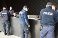 Na zdjęciu widać trzech policjantów stojących przy ladzie rejestracji w Szpitalu Tymczasowym MCK w Katowicach.