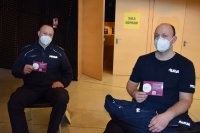 Na zdjęciu widać dwóch siedzących na krzesłach policjantów. Mundurowi trzymają w dłoni ulotkę Covid-19.